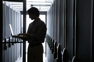 Technician with laptop, checking aisle of server storage cabinets in data center